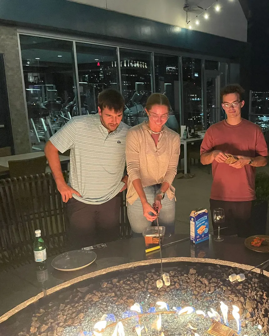 Friends making s'mores around a rooftop fire pit at night